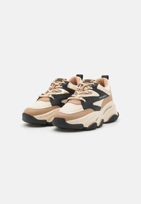Sneakers robusti con una combinazione di colori beige e nero. Realizzati con materiali misti, presentano una superficie testurizzata, una collo imbottito e suola in gomma.