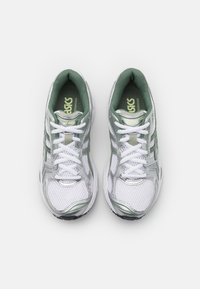 White athletic shoes with green accents. Mesh upper with silver detailing, round toe design, and laces. Features padded tongue and insole.