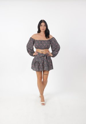 Bloemrijke crop top met elastische off-shoulder ontwerp, gecombineerd met een bijpassende flared rok met een strik in de taille, in zwart en roze.