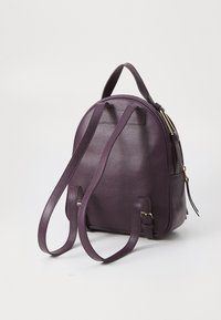 Sac à dos en cuir violet avec un design arrondi, surface texturée, bretelles réglables et accents en métal doré. Dispose d'une poche latérale.