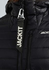 Svart puffjacka med en vadderad design, utrustad med en silverfärgad dragkedja och en svart tygdragtablå märkta "JACK1T" med vita bokstäver.