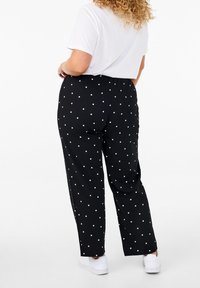 Svarta byxor med vita prickar, elastisk midja, rak ben-design, bärs med en vit t-shirt och vita sneakers.