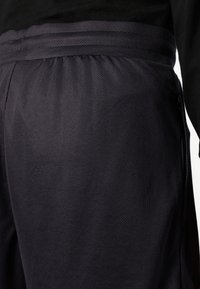 Shorts de sport noirs en tissu maillé texturé, dotés d'une taille élastique et de poches latérales, avec une coupe ajustée.