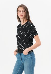 Black short-sleeve t-shirt with white polka dots, ribbed texture, round neckline, and slim fit, paired with light blue jeans.