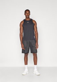 Schwarzes Sporttanktop, schwarze Mesh-Shorts und weiße Sneaker. Hat ein Logo auf der Brust und strukturiertes Material an den Shorts.