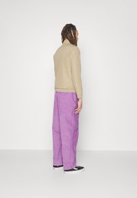 Giubbotto bomber beige con polsini elasticizzati, abbinato a pantaloni in corduroy leggeri di colore violaceo e sneakers nere con dettagli bianchi.