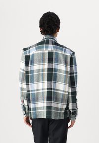 Plaid shirt with green, blue, and white tones, featuring a textured fabric and buttoned cuffs, designed with a relaxed fit and back yoke.