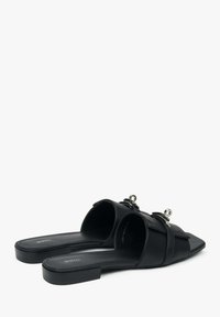 Zwarte leren slipper sandalen met platte hak, open teen en decoratieve metalen accenten op de banden; textuur zool voor grip en comfort.
