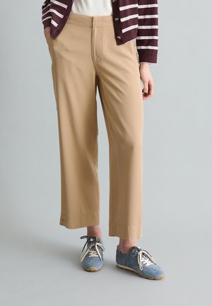 Osoba ubrana w beżowe spodnie o szerokich nogawkach, niebiesko-szare tenisówki z białymi sznurowadłami oraz bordowo-biały kardigan w paski, na białej bluzce.