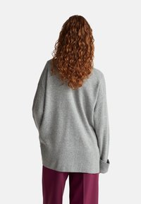 Světle šedý oversized svetr vyrobený z měkké látky, s širokým ribovaným lemem a uvolněným střihem. Jednoduchý design bez vzorů.