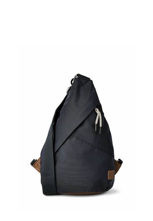 Mochila tipo bandolera negra con correa de hombro ajustable, bolsillo frontal con cremallera y parche de cuero marrón con el logo en la esquina inferior.