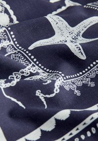 Tissu bleu foncé avec étoiles de mer blanches et motifs complexes de bordures semblables à de la dentelle, présenté avec des plis doux et des détails de texture.