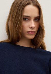 Marineblauer Strickpullover mit rundem Ausschnitt, feiner Textur und lockerer Passform, getragen von einer Person mit langen, glatten braunen Haaren und neutralen Gesichtszügen.