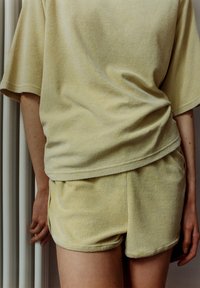 Geel terrycloth loungewear set, met een losse korte mouwen top en bijpassende shorts, beide met een zachte textuur en een casual ontwerp.