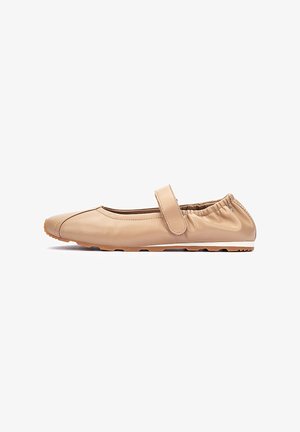 Zapato plano beige con parte trasera elástica, correa ajustable en la parte superior y suela de goma con dibujo para agarre.