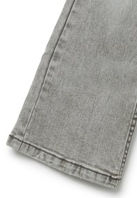 Grijze denim stof die de zoom en zijnaad van een broekspijp toont met zichtbare stiksels en subtiele textuur.