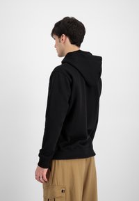 Zwarte hoodie met een voorste kangoeroezak, ribbelmanchetten en -zoom. Heeft een ruime capuchon en een relaxte pasvorm. Gecombineerd met beige cargobroek.