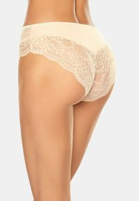 Beige Spitzenunterwäsche mit floralem Muster, ausgestattet mit einem glatten Bund und gewellten Kanten, die eine zarte, durchsichtige Textur betonen.