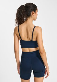 Haut court de sport bleu marine avec bretelles ajustables et short taille haute. Le matériau semble lisse avec une coupe ajustée et des détails de couture minimalistes.