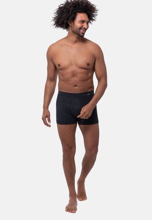 Schwarz gestreifte Boxershorts aus weichem Stoff, mit einem bequemen Bund und einer figurbetonten Passform, getragen von einem Mann mit lockigem Haar.