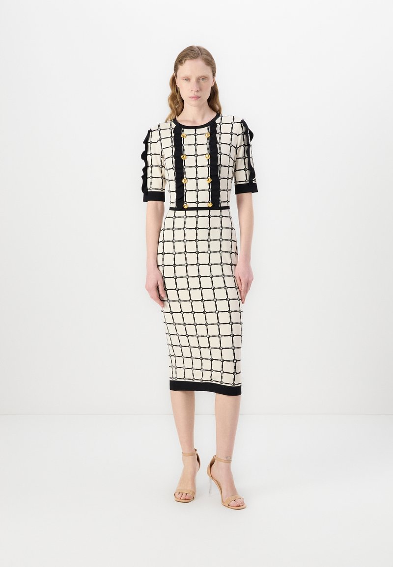 Rochie până la genunchi, de culoare crem, cu un model de grilă neagră, mâneci scurte fâlfâite și nasturi aurii pe față. Textură netedă. Poală neagră.