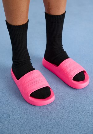 Feet wearing black socks with bright pink textured slide sandals on a blue carpeted floor.