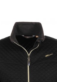 Veste matelassée noire avec un col haut, fermeture éclair et doublure en polaire marron. Accent logo doré sur la poitrine. Étiquette de taille visible.