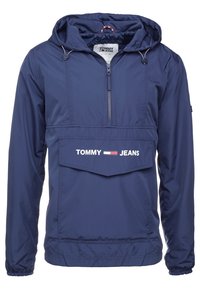 Marinblå vindjacka med huva, dragkedja framtill och stor framficka. Har "TOMMY JEANS"-logotyp i vitt. Slät, lättviktig tyg.