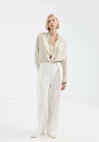 Luźna, kremowa koszula w pionowe paski, zestawiona z białymi, szerokimi spodniami z wysokim stanem. Prosty akcent w postaci złotego łańcuszka.