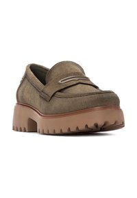 Mocasines de ante marrón con puntera redondeada, adorno de silla y suela de goma gruesa con dibujos pronunciados para mayor agarre.