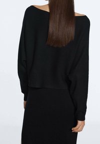 Pull en maille côtelée noire avec un large décolleté et des épaules tombantes, associé à une jupe ajustée assortie, vu de dos.