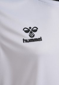 Vit sporttröja med en slät textur, försedd med en svart "hummel"-logotyp och en stiliserad biikon på vänster bröstområde.