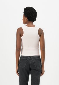 Canotta a costine di un leggero rosa chiaro con scollatura rotonda e spalline larghe, abbinata a jeans a vita alta di un grigio scuro con tasche posteriori.