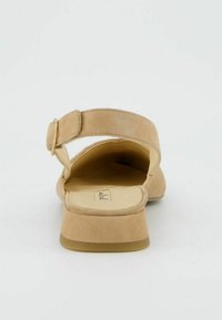 Béžové semišové sandály se širokým páskem a přezkou, plochou podrážkou a zaoblenou špičkou. Hladký povrch, jednoduchý design.