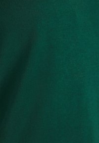 Tissu vert foncé avec une surface lisse et légèrement texturée. Le matériau semble être du coton ou un mélange de coton, présentant une répartition uniforme de la couleur.