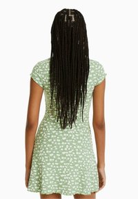 Vihreä kukallinen mekko lyhyillä hihansuilla ja istuvalla vartalonmyötäisellä korissa. Varustettu leijailevalla hameella sekä teksturoidulla kankaalla, jossa on pieniä valkoisia kukkakuosisia kuvioita.