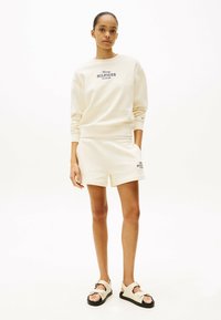 Crème sweatshirt en short set met het "Tommy Hilfiger" logo in donkerblauw. Het sweatshirt heeft geribbelde manchetten; de shorts hebben een relaxed fit. Lichtbruine sandalen.