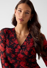 Bloemen wikkeljurk met lange mouwen. Heeft een zwarte basis met rode bloemen. Zachte stof met een diepe V-halslijn en een aangesloten silhouet.