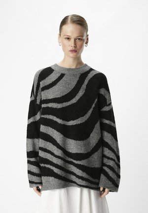 Pull en laine grise floue avec des rayures noires en spirale, col rond, manches longues et coupe décontractée. Le matériau semble doux et texturé.