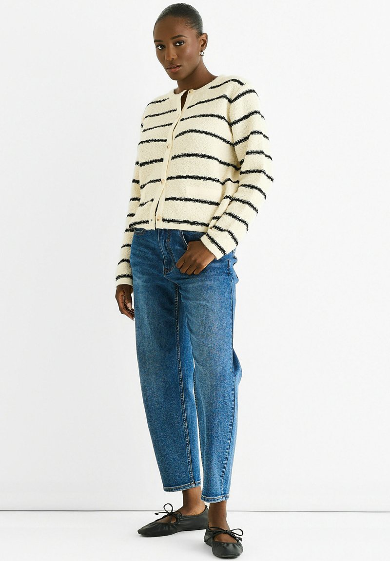 Striped cardigan in cream and black, textured fabric, round neckline, button closure, paired with blue straight-leg jeans and black flats.