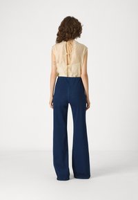 Beige sleeveless top with a tied back detail, paired with dark blue wide-leg trousers. Smooth fabric and loose fit enhance comfort.