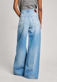 Jeans de corte ancho en denim azul claro, con una cintura alta, dos bolsillos traseros y un parche de cuero en la cinturilla. Textura suave.