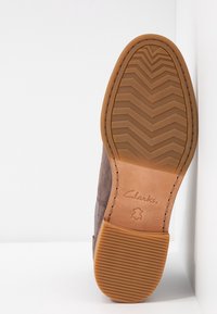 Semelle d'une chaussure en daim marron avec talon rainuré et motif de bande en chevrons, estampillée « Clarks » avec symbole de cuir sur la semelle intermédiaire.