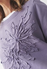 Felpa viola con design in appliqué testurizzato che ricorda i raggi del sole, colletto a girocollo bianco a contrasto e morbido materiale in cotone.