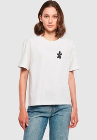T-shirt blanc à manches courtes en coton, avec un motif floral noir central. Coupe décontractée, encolure ronde et texture lisse.