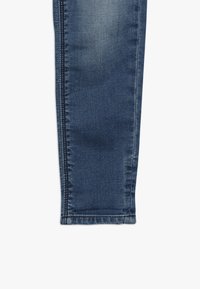 Tmavomodré džíny z denimu s hladkou texturou, slim fit a kontrastním šitím. Mají mírně vybledlý vzhled v oblasti kolen.