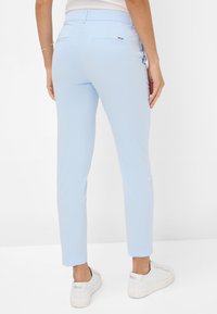 Lichtblauwe enkel-lange broek van gladde stof, met een achterzak en gecombineerd met witte sneakers.