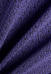 Tissu violet avec motif géométrique abstrait noir, présenté en gros plan sur des plis mettant en valeur la texture et les détails du tissage.