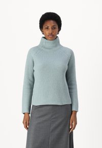 Light blue ribbed knit sweater with a high collar, long sleeves, and a slightly cropped hemline, paired with a gray skirt.