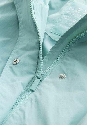 Šviesiai mėlyna, vandeniui atspari striukė su centrine užtrauktuku, spaudėmis ir lygiu paviršiumi. Yra etiketė su prekės ženklo informacija.